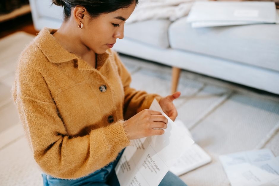 Young ethnic female in casual clothes sitting on floor while organizing sheets of paper