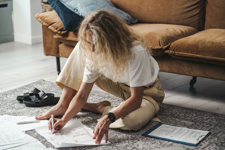 Woman sits on the carpet planning and drawing floor plans in a cozy living room.