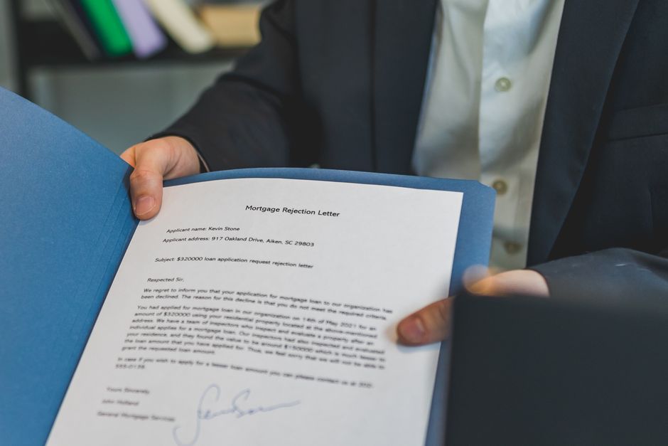 Close-up view of a person holding a mortgage rejection letter in a folder, indoors.